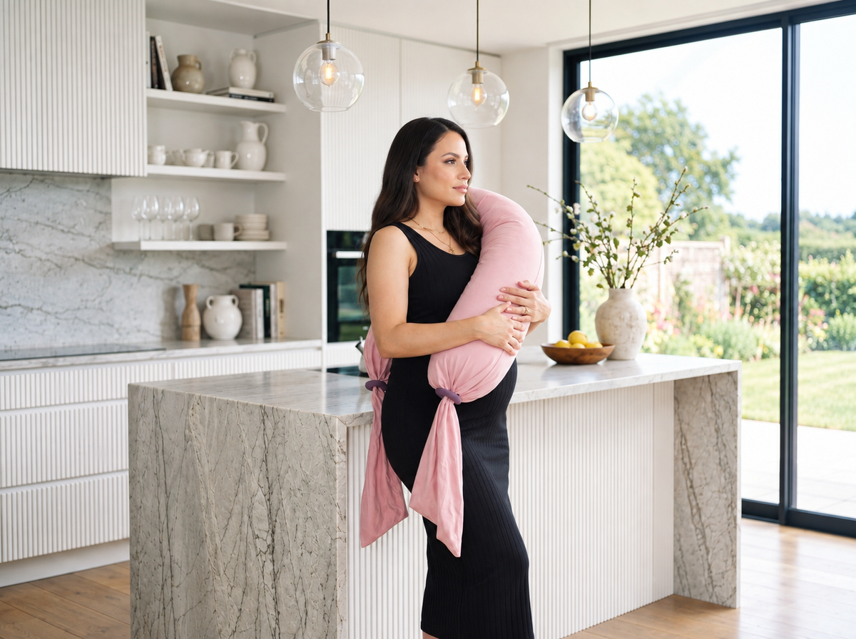 Femme enceinte debout dans une cuisine avec un coussin de grossesse rose