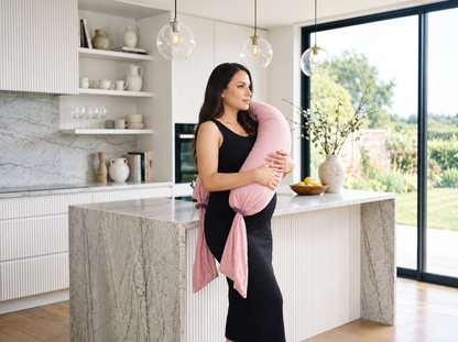 Femme enceinte debout dans une cuisine avec un coussin de grossesse rose