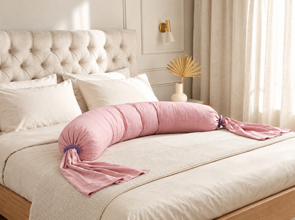 Coussin de grossesse et d'allaitement rose posé sur un lit