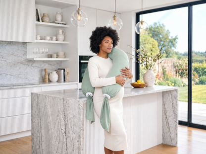 Femme debout dans une cuisine avec un coussin de grossesse vert