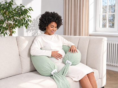 Femme assise sur un canapé avec un coussin de grossesse vert